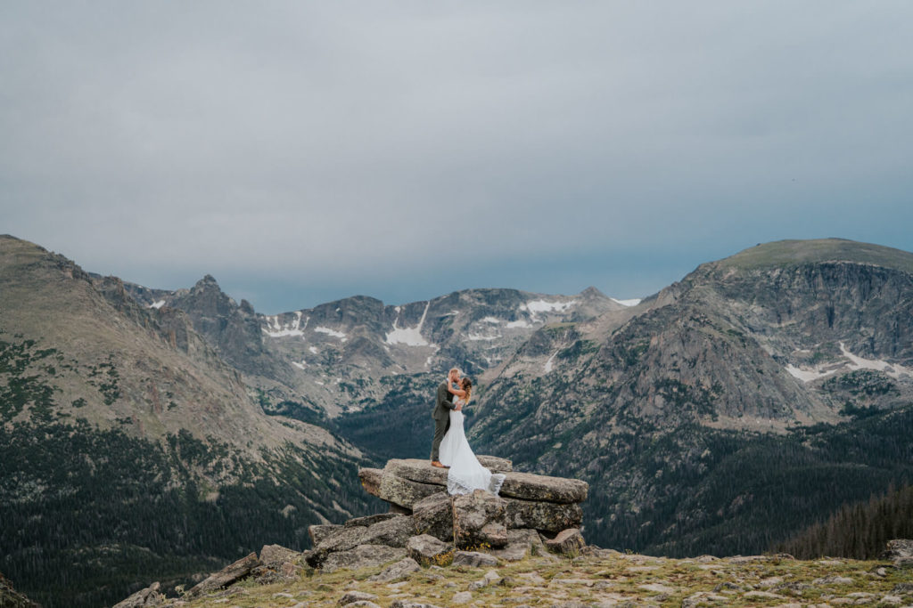 an epic shot of an eloping couple on a rock overlooking the Rcokies on Trail Ridge Road. 