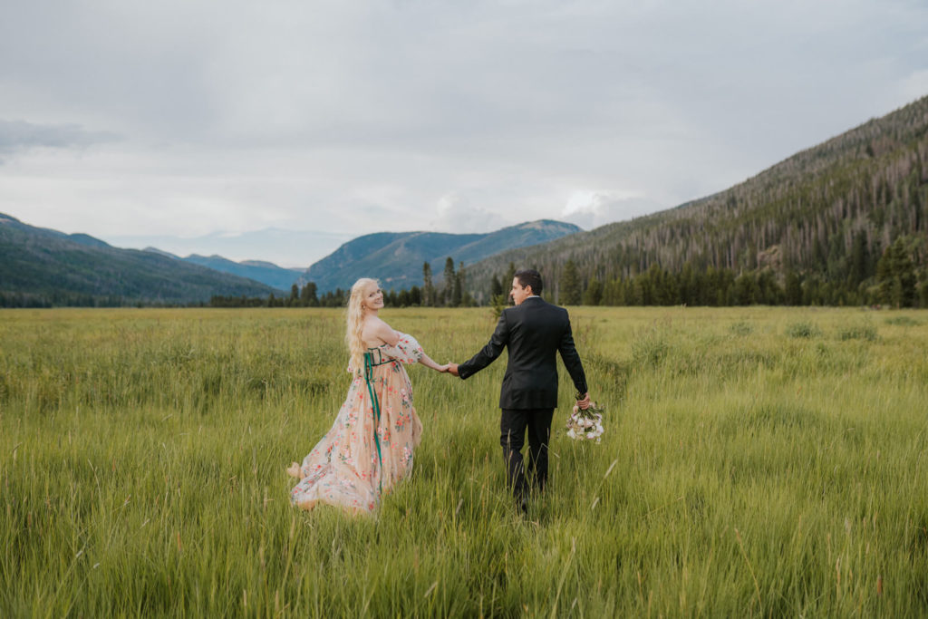 bride looking over her shoulder as her husband guides her through a meadow near Grand Lake, Colorado. 